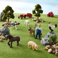 several farm animals are in the grass with rocks and trees around them, while a man is holding a shovel