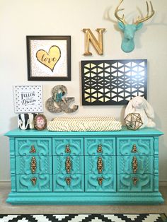 a turquoise dresser with gold accents and pictures on the wall next to an animal head