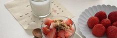 strawberries and other fruit are in bowls next to a glass of milk on a table