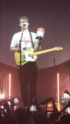 a man holding a yellow guitar while standing on top of a stage with microphones