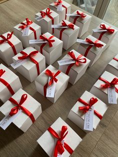 many white boxes with red bows and name tags on them sitting on a wooden table