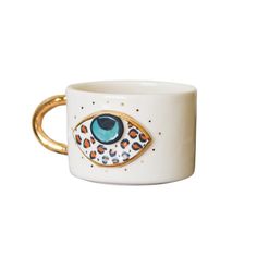 a white mug with an eye on it and gold handles, sitting in front of a white background