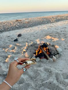 a person holding a piece of food in front of a campfire on the beach