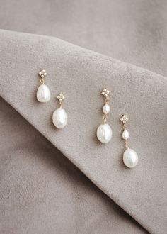 three pairs of pearl and diamond earrings sitting on top of a gray cloth with a white background