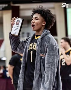 a young man holding up a plaque in front of his face while standing on a basketball court