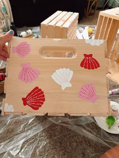 a person holding a wooden box with seashells painted on it