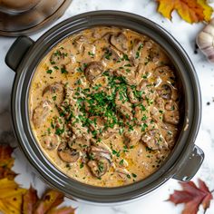 a stew with mushrooms and parsley in a crock pot on a white table