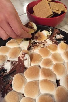 a person dipping marshmallows into a skillet filled with hot fudge