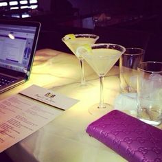 a laptop computer sitting on top of a table next to two martini glasses and a notepad