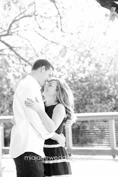 a man and woman standing next to each other under a tree in black and white