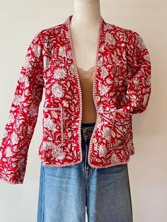 Indian Handmade Women's Quilt Jacket With Stripe Piping Looks Rich. Featuring a V-Neck button down, and two front pockets. Hand block printed in a vibrant red and white floral print. The contrast piping is a stand out. Beautiful. Styled in a short blazer jacket resting just below the waist. Long sleeves, fold back to expose the mixed print and piping, adjusting the sleeve length. This jacket should work well with your existing wardrobe. Great over skirts, crop pants, long pants, and even shorts. Red V-neck Cotton Outerwear, Red V-neck Outerwear With Button Closure, Red Cotton V-neck Cardigan, Red Buttoned Cardigan For Spring, Red Cotton Cardigan For Spring, Red Floral Print Winter Outerwear, Winter Red Floral Print Outerwear, Red Cotton Button-up Outerwear, Red Spring Cardigan With Button Closure