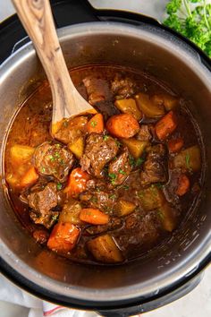 a pot filled with beef and carrots on top of a table next to a wooden spoon