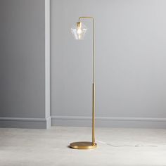 a floor lamp with a glass shade on the base and a gold metal pole, in an empty room