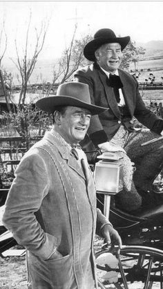 black and white photograph of two men in cowboy hats standing next to a horse drawn carriage