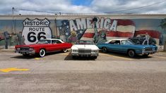 three old cars parked in front of a wall with an american flag painted on it