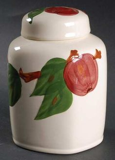 a white ceramic jar with a painted apple on the front and green leaves around it