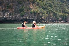 two people in a kayak paddling on the water near a rocky cliff face