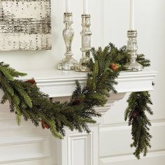 a fireplace mantel decorated with pine cones, candles and evergreen garland for christmas time