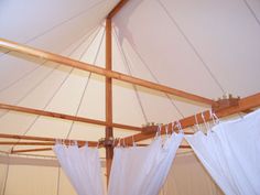 the inside of a tent with white curtains hanging from it's ceiling and wood beams