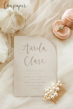 the wedding stationery is laid out on top of white tulle with pearls and gold hair combs