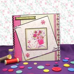 a greeting card with buttons and thread on the table next to it is a pink flowered background