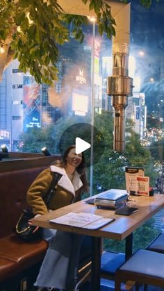 a woman sitting at a table in front of a window with a view of the city