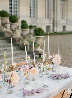 the table is set with candles and flowers in vases on it, along with other place settings