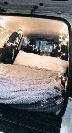 the back end of a white van with lights on it's bed and pillows