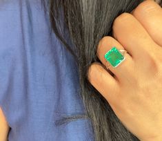 Introducing our Phalgun Emerald Adjustable Statement Ring, a stunning piece of jewelry that showcases the beauty of lab-grown emeralds. This ring features a large, vivid green emerald, capturing the essence of the lush green forests and bringing a pop of color to any outfit. The emerald is a lab-grown stone, ensuring that it is ethically sourced and environmentally friendly. This ring is the perfect cocktail ring, making a statement at any special occasion. The adjustable design allows for a comfortable fit, ensuring that the ring stays in place no matter what the night brings. The emerald is associated with the Anahata chakra, known for its ability to bring balance and harmony to the mind and body. Wearing this ring is not only a fashion statement, but also a way to tap into the spiritual Green Emerald Ring With Accent Stones For May Birthstone, Green Emerald Rings With Accent Stones, Green Emerald Cut Ring With Accent Stones, Gia Certified Green Emerald Ring In Fine Jewelry Style, Fine Jewelry Green Emerald Ring With Accent Stones, Emerald Jewelry With Accent Stones, Green Emerald Jewelry With Accent Stones, Emerald Green Jewelry With Accent Stones, Emerald Cut Green Emerald Ring For May Birthstone