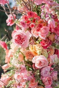 an arrangement of pink and orange flowers in a vase with greenery on the side