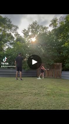 two people are playing frisbee in the yard with trees and bushes behind them