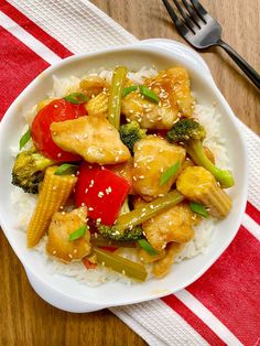 a white plate topped with chicken and veggies on top of rice next to a fork