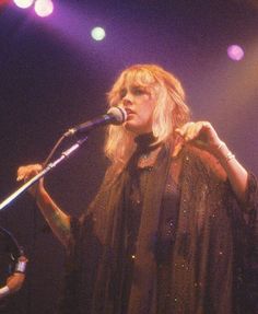 a woman standing in front of a microphone on top of a stage with lights behind her