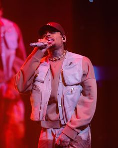 a man standing on top of a stage with a microphone in his hand and wearing a baseball cap