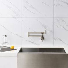 a stainless steel sink in a white kitchen with marble walls and flooring, next to a towel dispenser