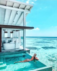 a man swimming in the ocean next to a beach house with an open air jacuzzi