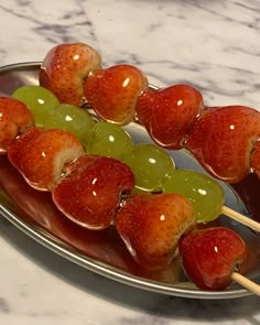 grapes and strawberries are being served on skewers with green apples in the background