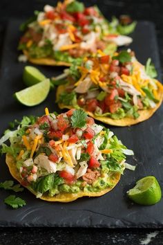 three tortillas topped with chicken, lettuce and salsa on a black tray