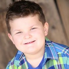 a young boy is smiling and wearing a blue shirt with green checkered shirts on