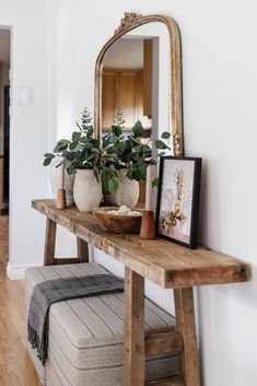 a wooden table topped with a mirror and potted plant next to a bench in front of a doorway