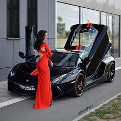 a woman in an orange dress standing next to a black sports car