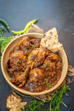 a wooden bowl filled with chicken curry and pita chips on top of a table