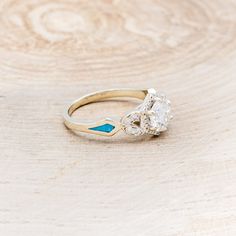 a diamond and blue enamel ring sitting on top of a piece of plywood wood