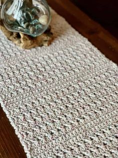 a glass vase sitting on top of a wooden table next to a white crocheted rug