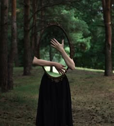 a woman with her hands on the mirror in front of her face, and trees behind her