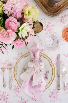 the table is set with pink and white flowers, silverware, and napkins