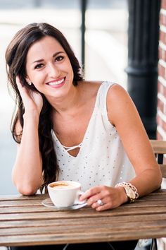 a woman sitting at a table with a cup of coffee in her hand and smiling