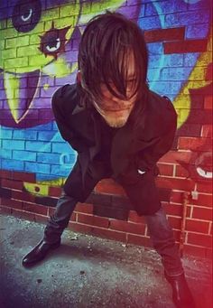 a man with dreadlocks leaning against a brick wall