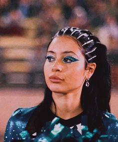 a woman with long hair and blue eyeshadow looks off to the side in front of an audience