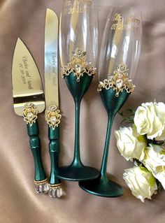 three wine glasses and a knife on a satin table cloth next to white flowers with gold trimmings